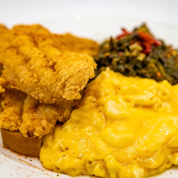 Fried catfish fillets with creamy macaroni and cheese and a side of collard greens.