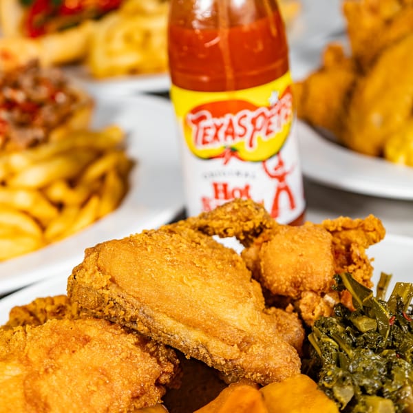 Crispy fried chicken with collard greens and sweet potatoes, with a bottle of Texas Pete hot sauce.