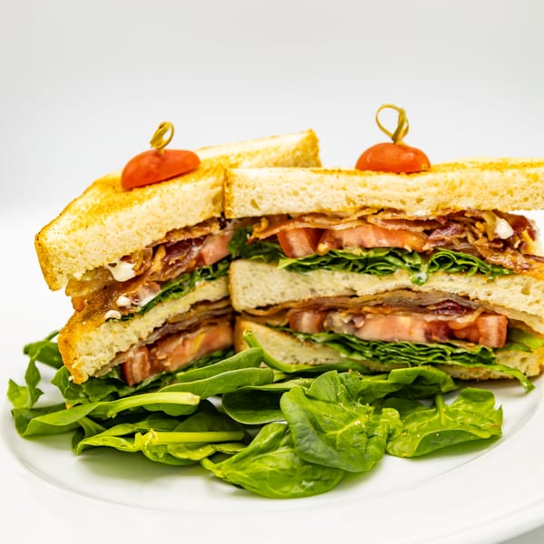 A Selby's Grab and Go club sandwich with bacon, lettuce, and tomato, served with fresh greens.